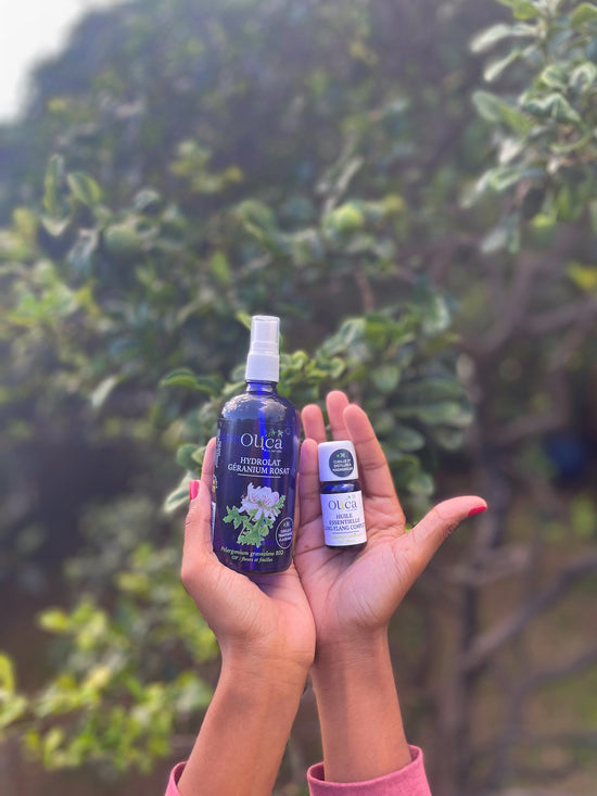 Une main portant un hydrolat de Géranium Rosat et une huile essentielle